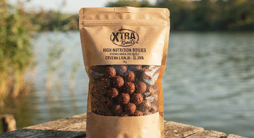 Close up photograph of dark reddish brown high nutrition boilies carp fishing baits texture inside craft packaging with warm natural lake light