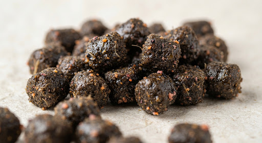 Dark oily premium carp feed pellets with krill meal, micro texture macro photography, natural paper background.