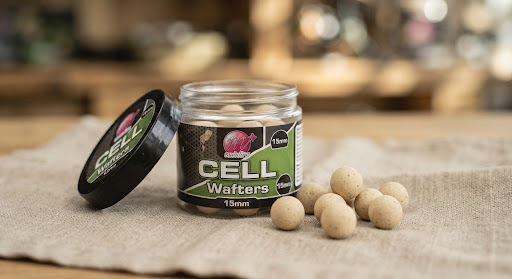 Mainline Cell Wafters 15mm round carp hookbaits presented in their signature branded tub with a few neutral-colored wafters resting outside on a rough linen cloth, clean aesthetic angler photography with shallow depth of field.