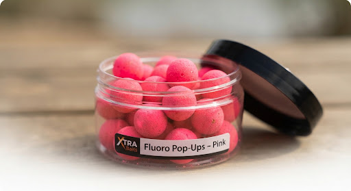 Vibrant fluorescent pink pop up carp boilies sitting in container, bright contrast fishing bait, editorial lighting.