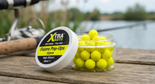 High contrast photograph of bright fluorescent yellow pop-up fishing bait pellets in acrylic tub with soft outdoor lighting