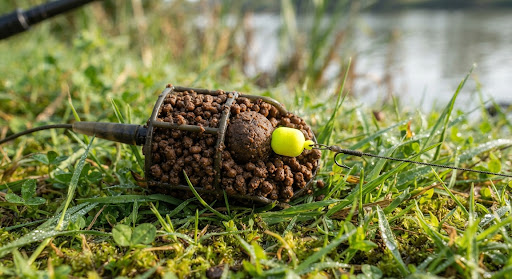 Method feeder cage loaded with micro pellets and a fluorescent yellow wafter hookbait, close-up shot on riverbank grass