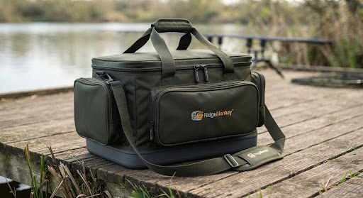 Rigid waterproof tackle duffel carryall bag in dark olive green by RidgeMonkey sitting on wooden bankside.